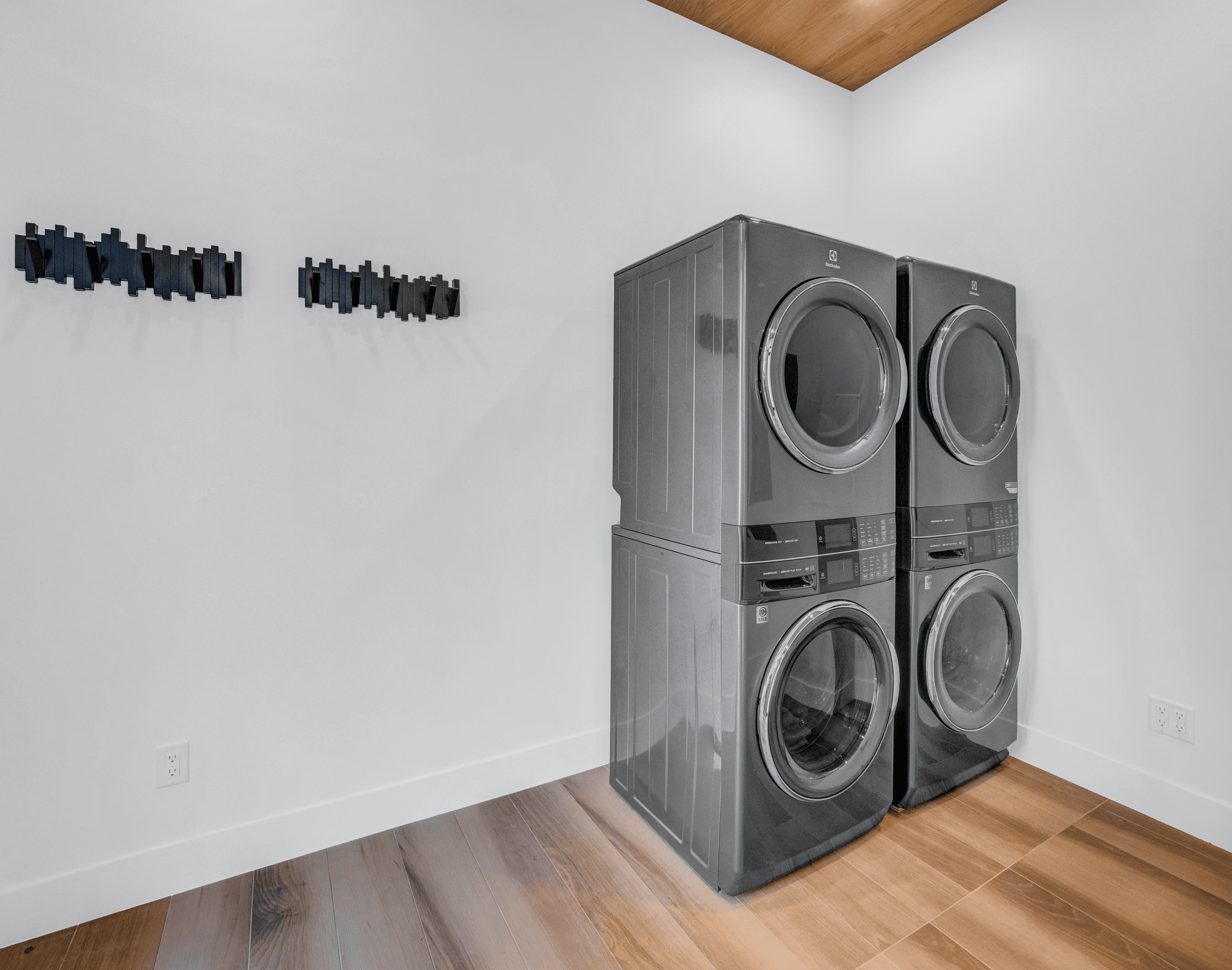 Modern laundry room featuring high-end stacked front-load washer and dryer with minimalist wall hooks and wood flooring
