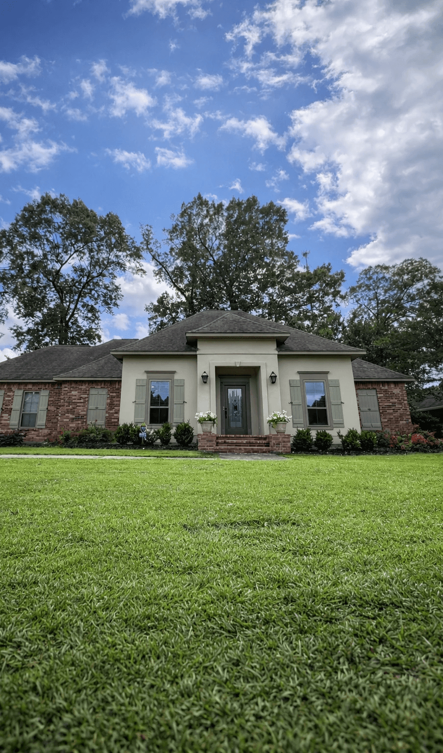 A modern, glass-walled house with warm interior lighting is perched on a rocky cliff overlooking a calm sea at sunset, under a clear blue sky.