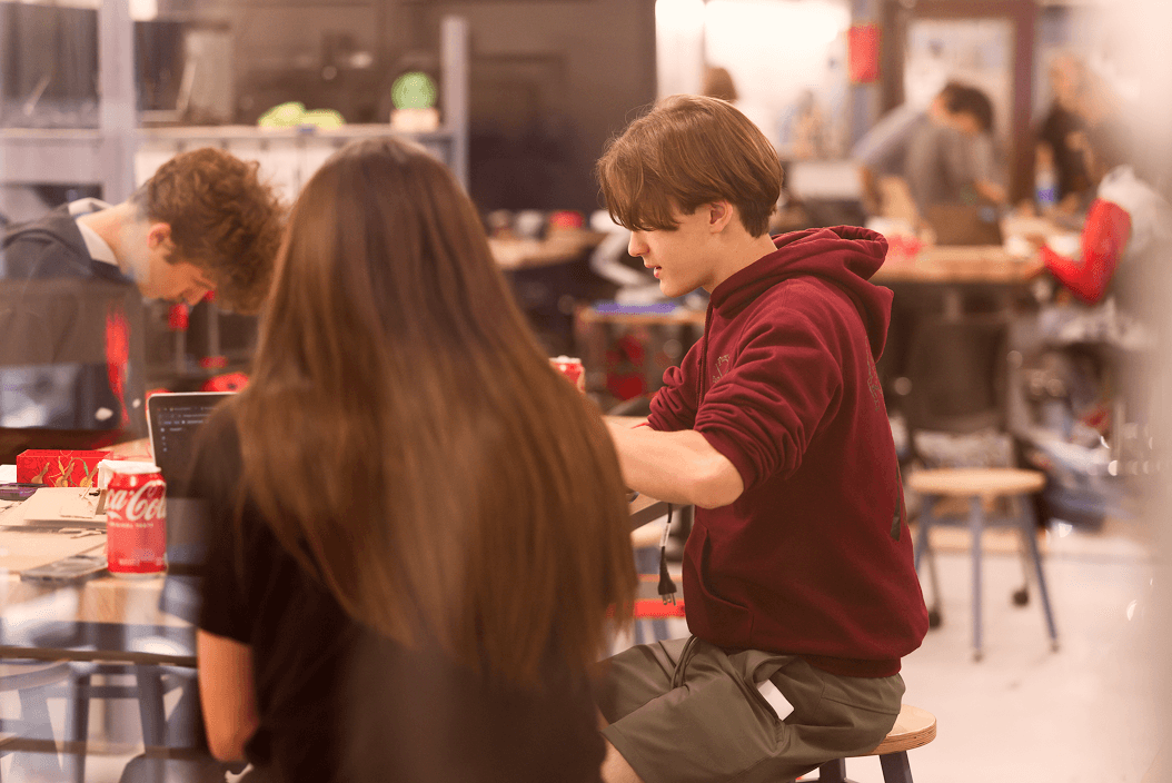 Students gathered around a table in a classroom, working together on a hands-on project.