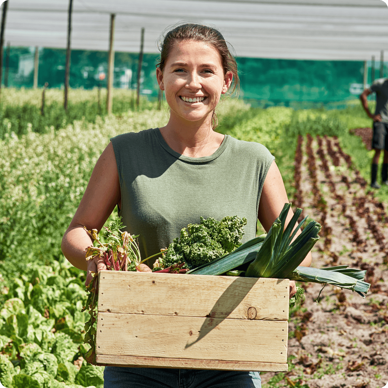 Fermière souriante tenant une caisse de légumes frais.