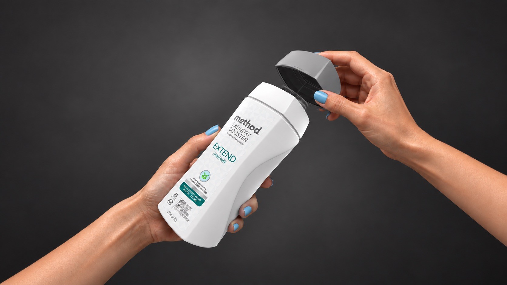 Hands with blue nail polish twisting the gray cap off a white laundry booster bottle against a dark gray background