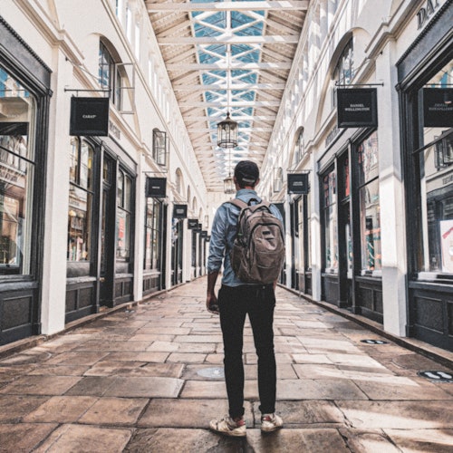 一个背着背包的人走在室内购物拱廊，拱廊有玻璃天花板和装饰性灯笼。