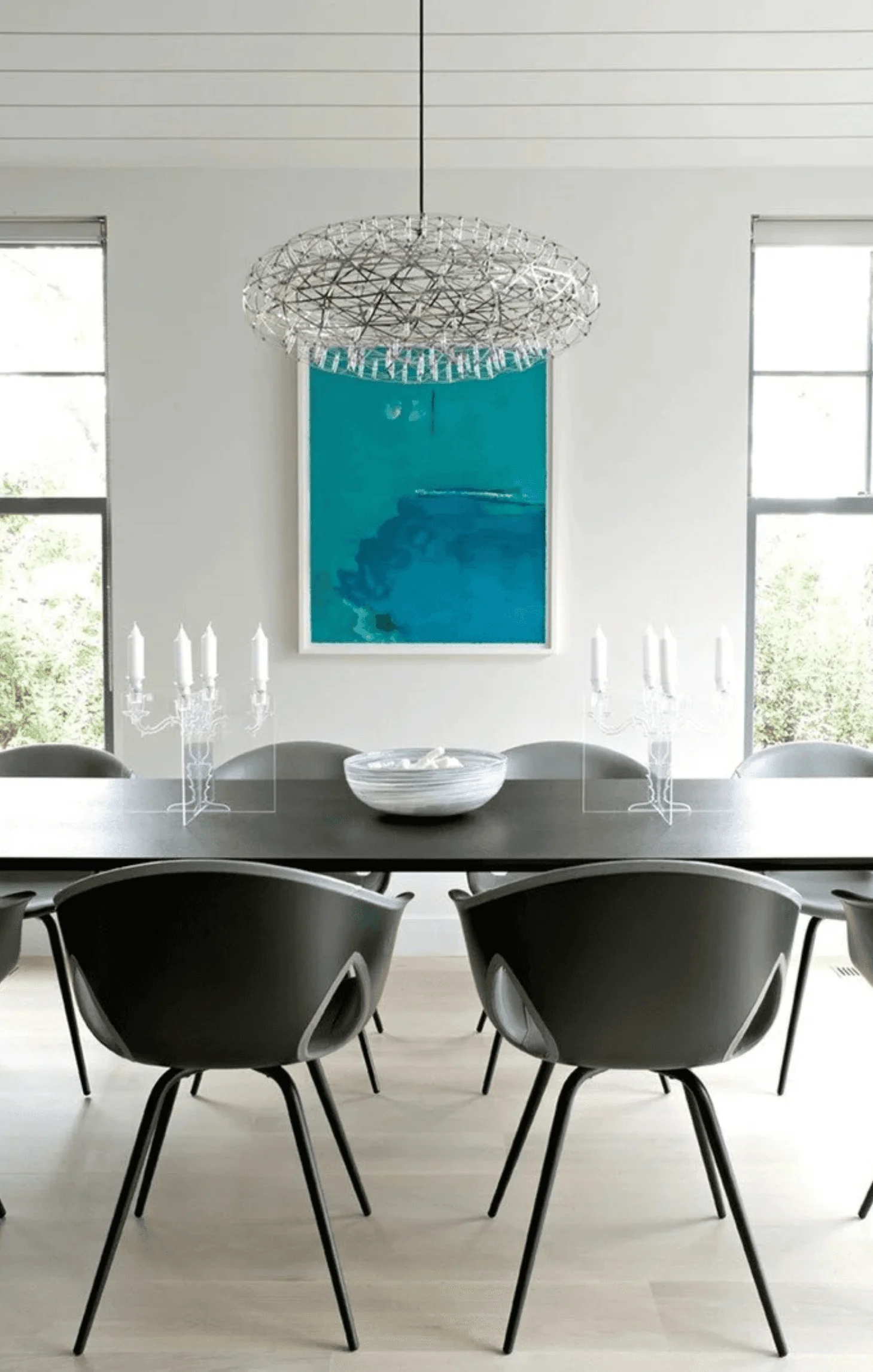 A closer view of the dining table, set with a ceramic bowl and flanked by candelabras beneath the wire chandelier
