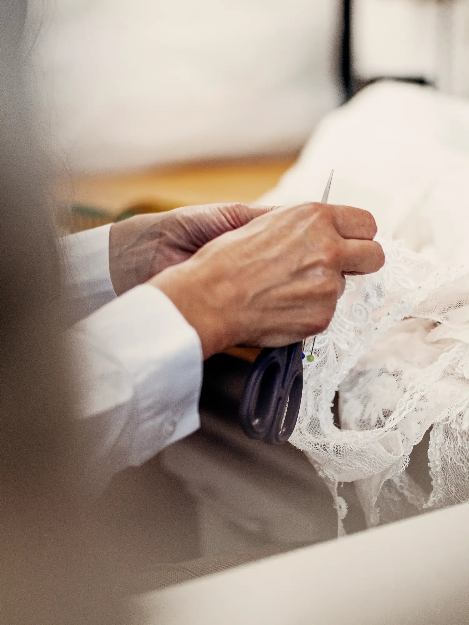 Detailaufnahme der traditionellen Handarbeit bei Kerst Hochzeitsmode: Erfahrene Hände bearbeiten mit Schere und Stecknadeln ein filigranes weißes Spitzenbrautkleid im hauseigenen Atelier.