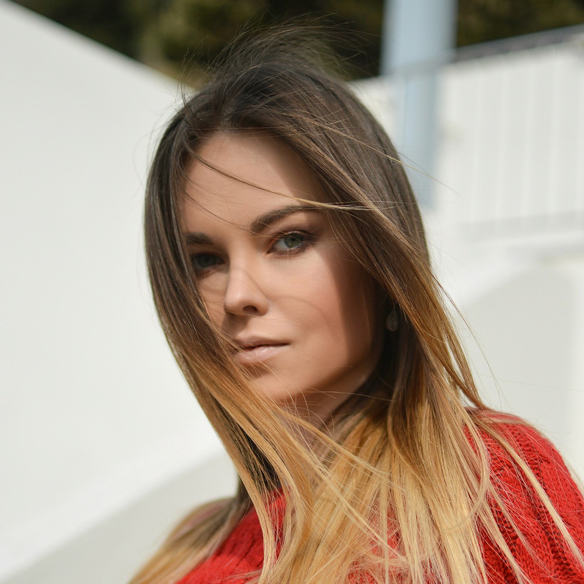 A portrait of a woman with long, straight blonde and brown hair wearing a red top.