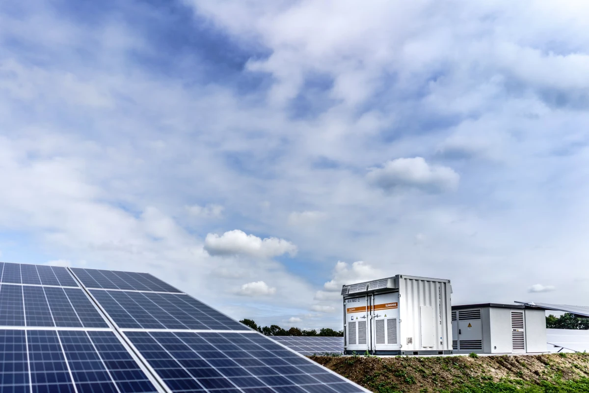 Solar panels and battery storage units under a cloudy sky.