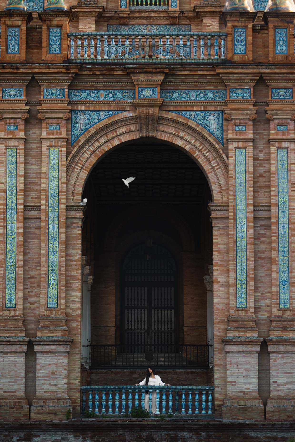 Girl standing under an arch with a bird flying at the edge of the arch in Plaza de Armas, Seville, Spain.