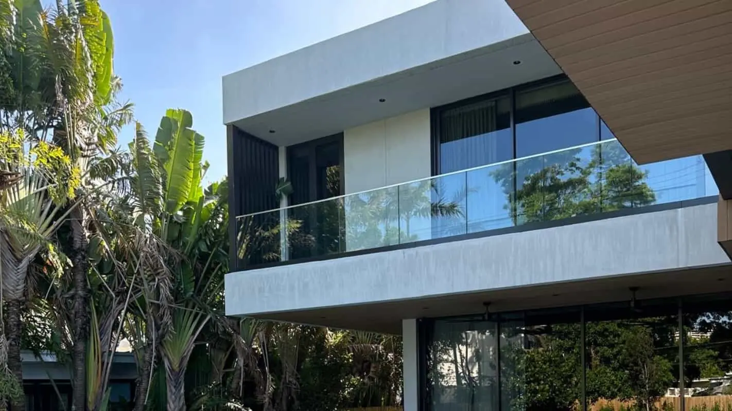 Rear exterior of Meridian Avenue Residence in South Beach — concrete upper volume with glass-railed balcony, floor-to-ceiling windows, and tropical landscaping including bird-of-paradise plants, by Atelier International.