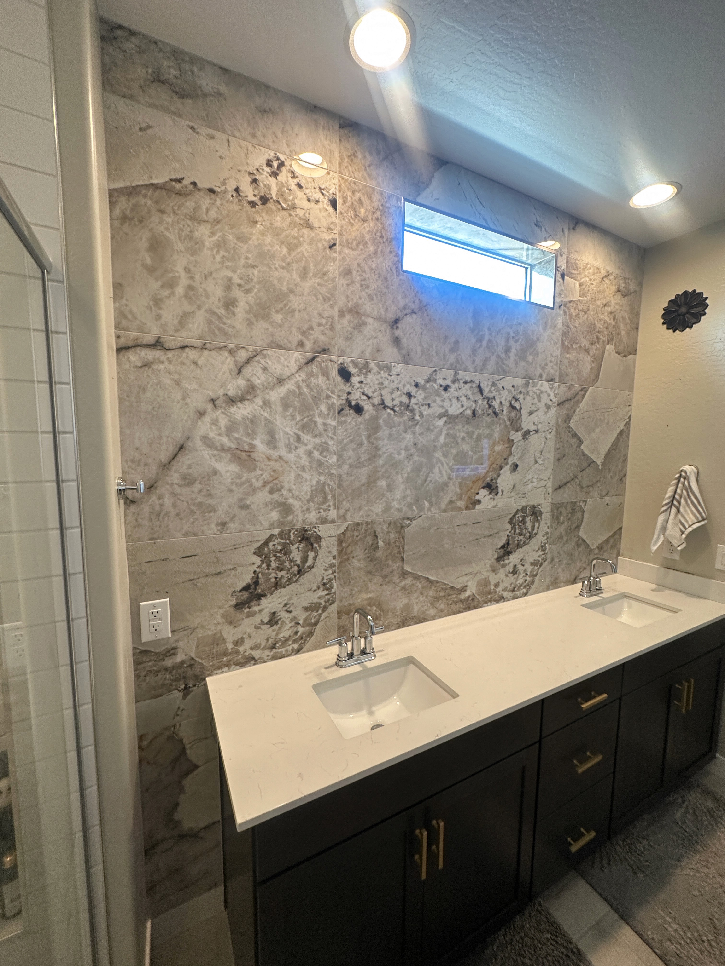 Luxurious bathroom vanity area with a dramatic wall featuring large format natural stone tiles in varying earthy tones and complex veining, serving as a striking backsplash above a double sink vanity.