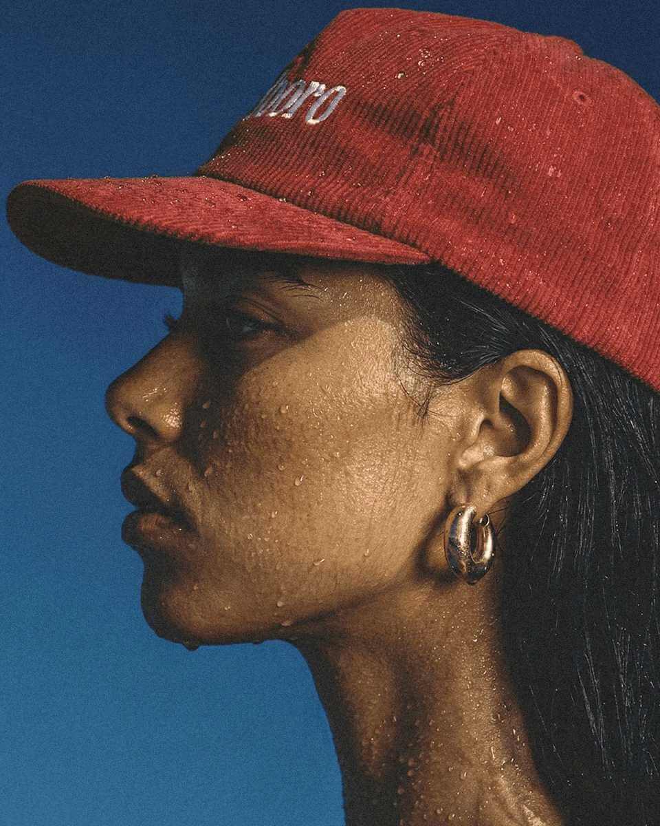 Close-up of a person in a red cap with water droplets on their skin, set against a blue background, showcasing vibrant contrast and detail.