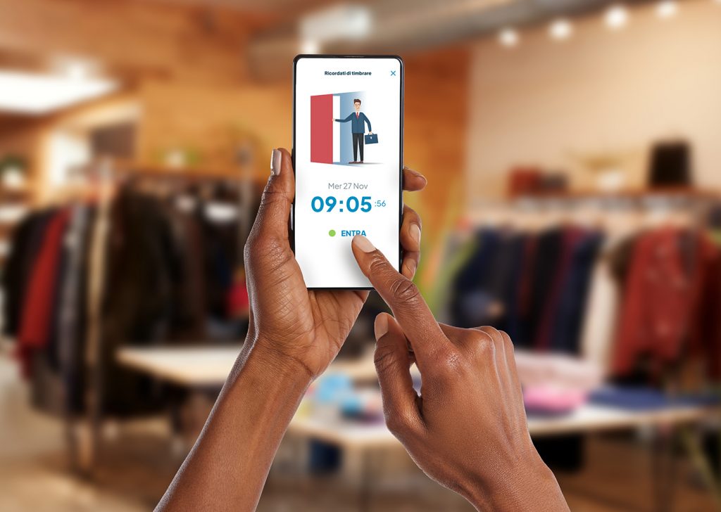 All’interno di un punto vendita vediamo una mano mentre clicca su “Entra” dalla schermata Fluida dell’app aperta sul suo smartphone