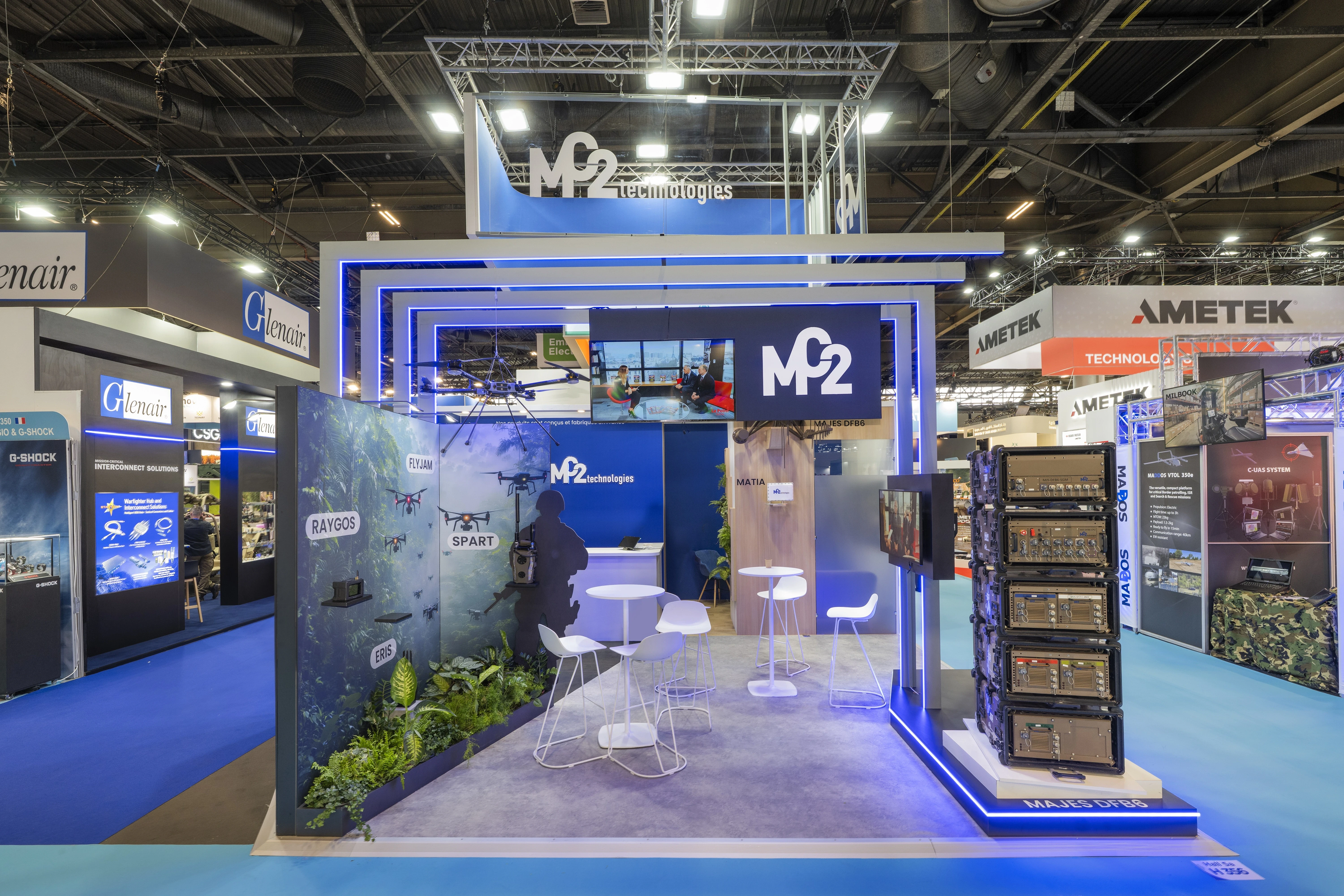 Stand MC2 Technologies lutte anti-drone conçu par EXPACE à Eurosatory 2026, Hall 5A — tour de brouilleurs MAJES DFB6 sur socle lumineux, mur jungle immersif et drones suspendus