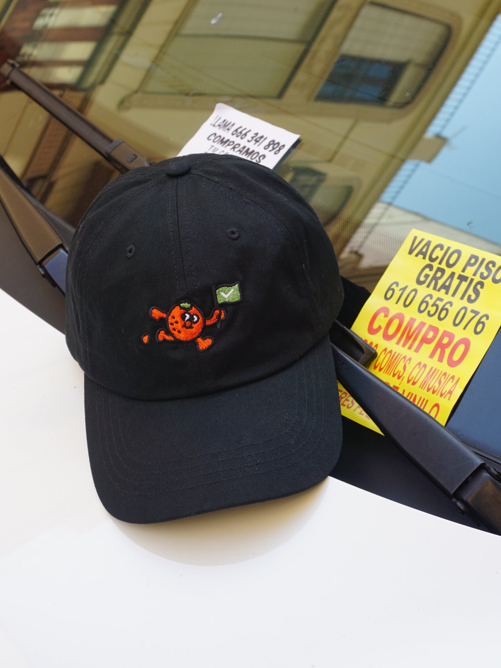Black cap with an orange fruit design on a car dashboard with a yellow flyer in the background.
