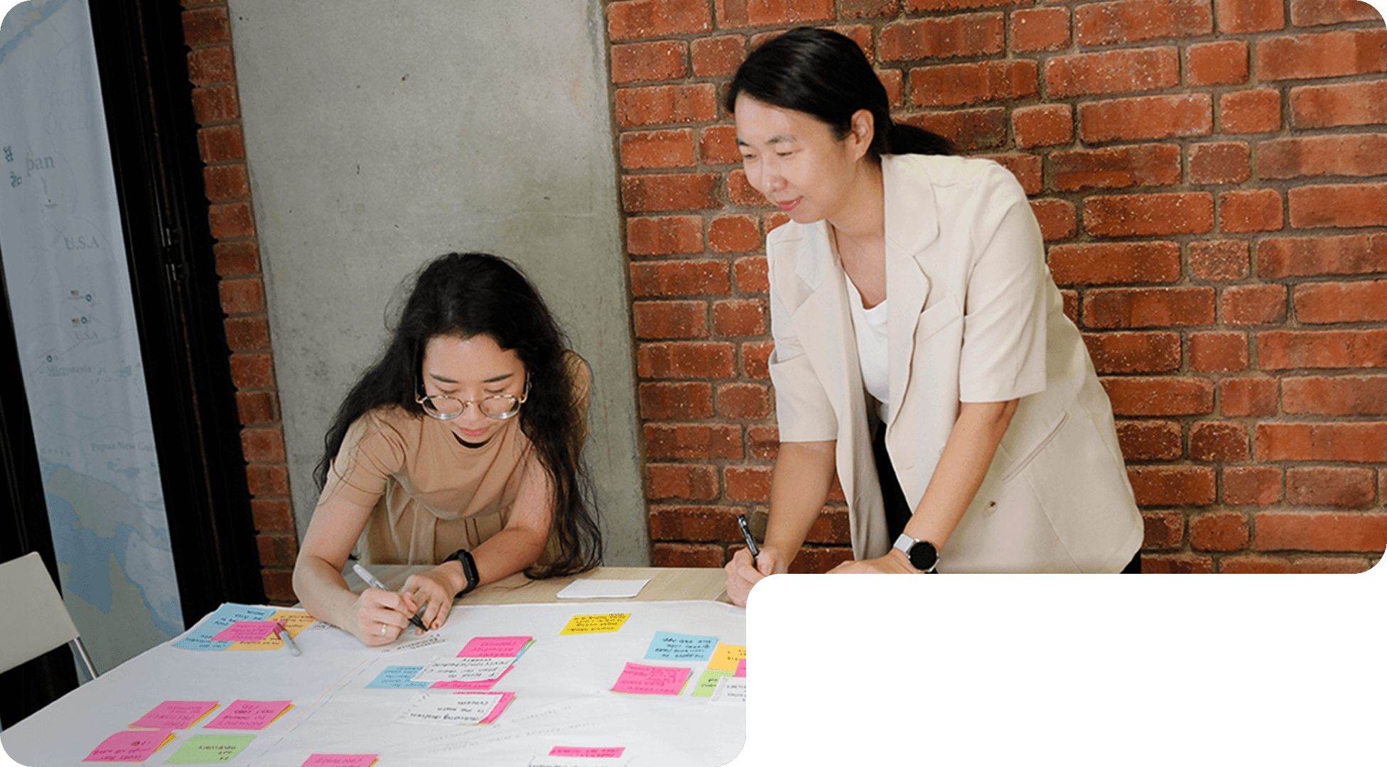 Two members of 55 Minutes collaborating at a table, writing on a large sheet filled with colorful sticky notes.