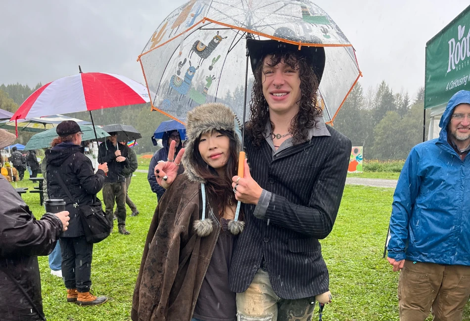Two people smiling and posing under a clear umbrella during a rainy Fall Farm Fest at Rooted Northwest.