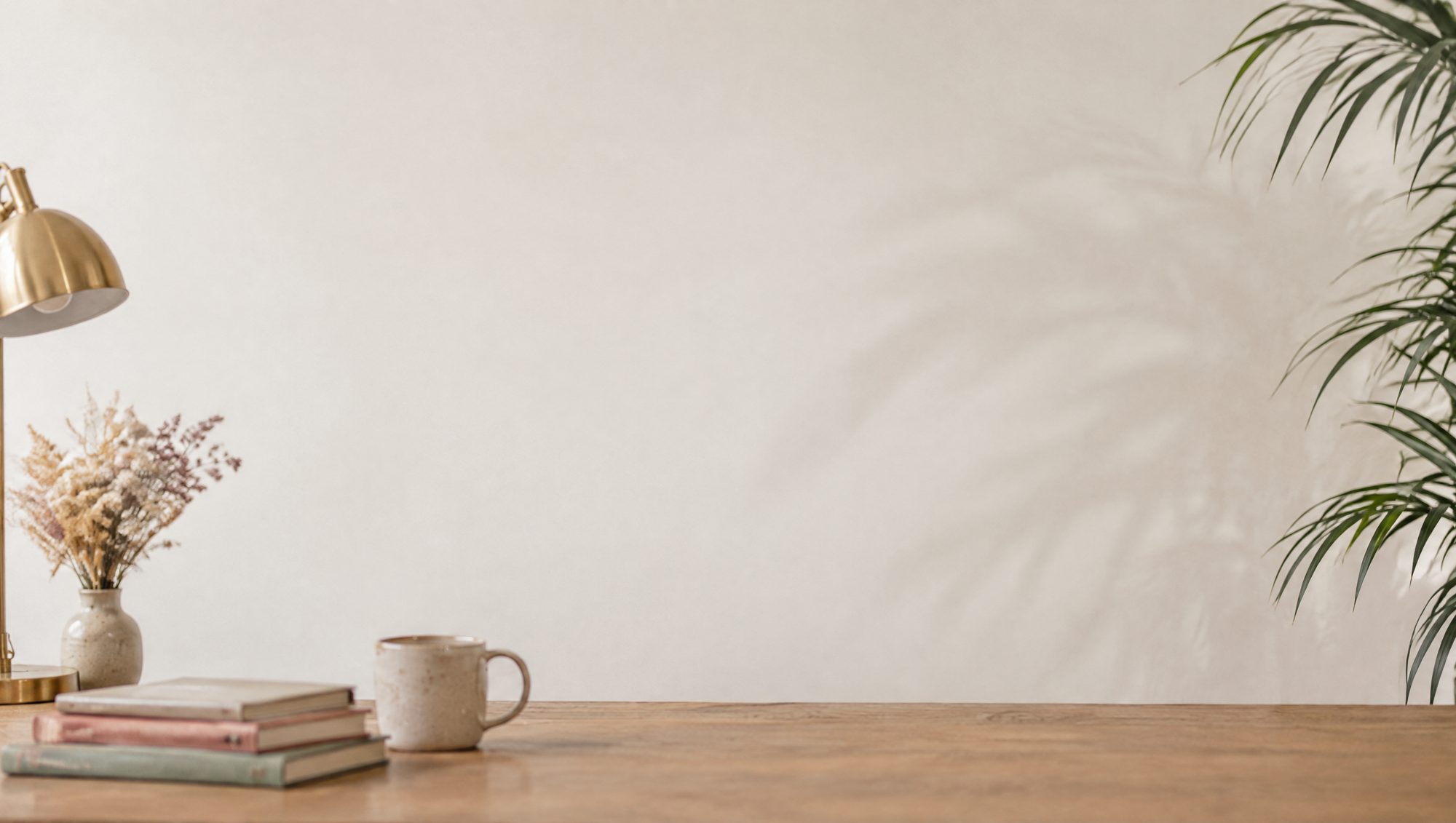 The oak desk with notebooks, a mug and dried flowers against a plain wall.