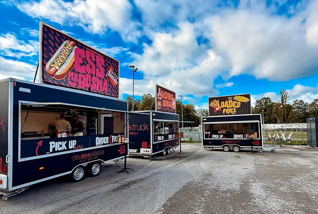 A food truck illuminated from within, showcasing a variety of food and drink items against a dark backdrop.