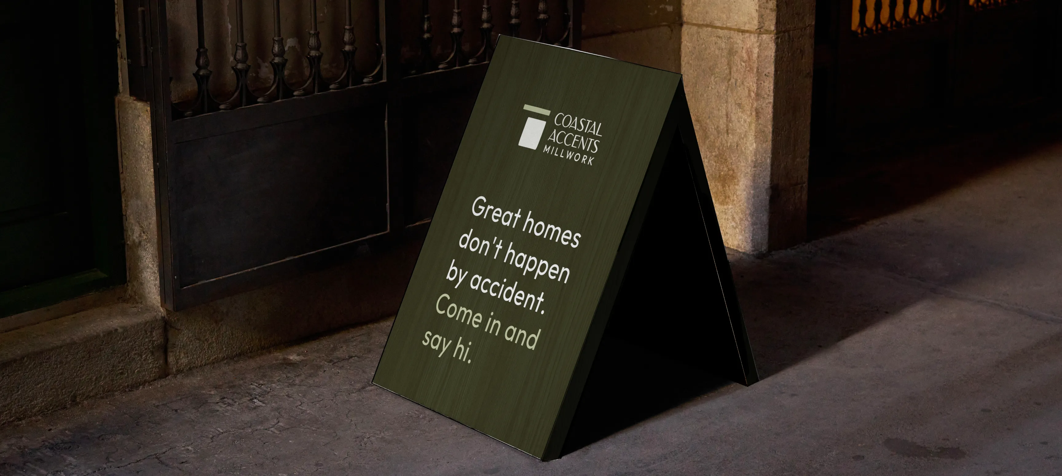 A sandwich board on a street with the Coastal Accents logo and the text "Great homes don't happen by accident. Come in and say hi."