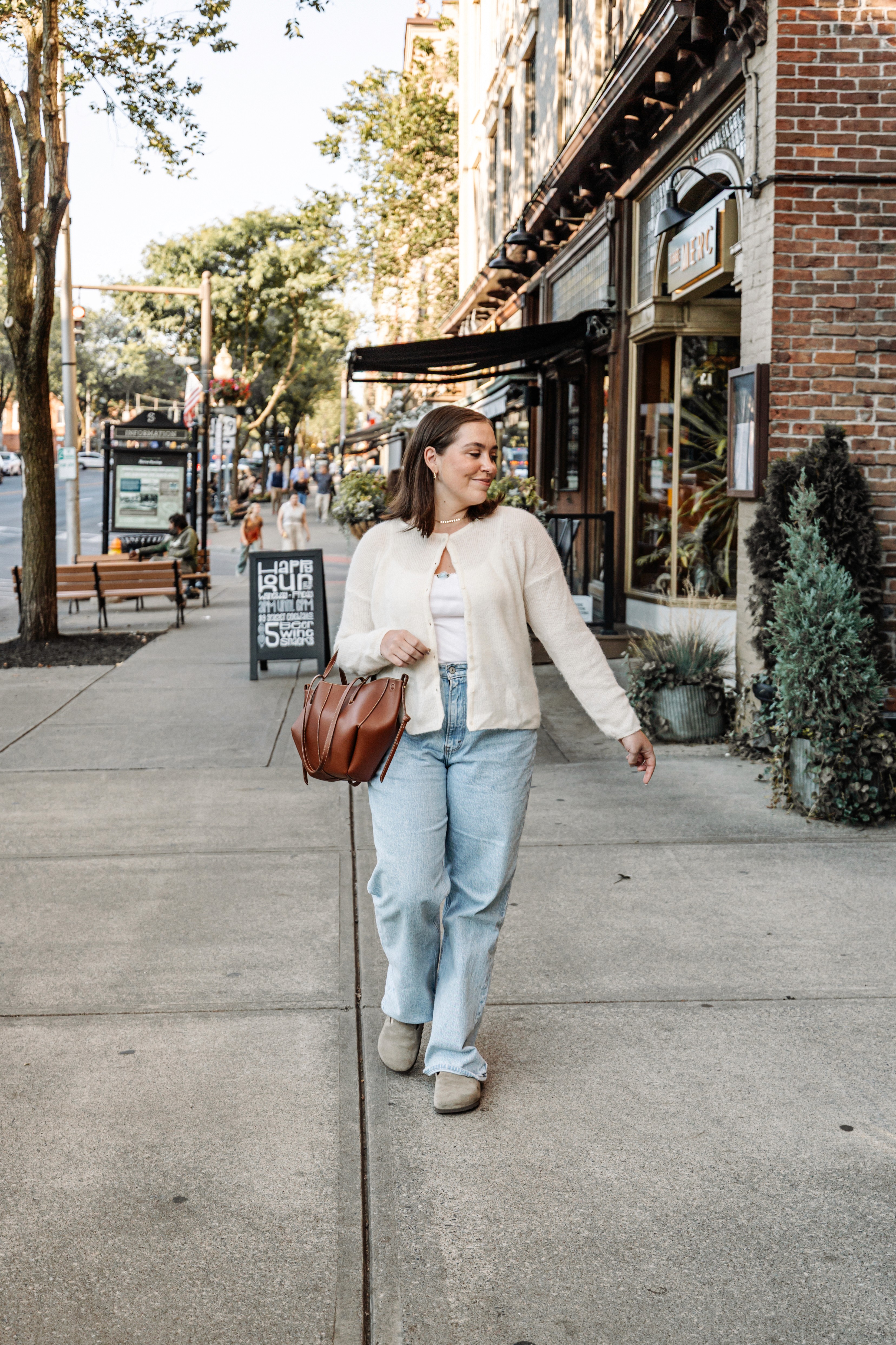 Stylish influencer on Broadway in downtown Saratoga Springs, hands in her hair, looking directly at the camera in a chic fall outfit — bold editorial lifestyle and content creator photography by Lizz Spano Photography, Saratoga Springs lifestyle photographer.