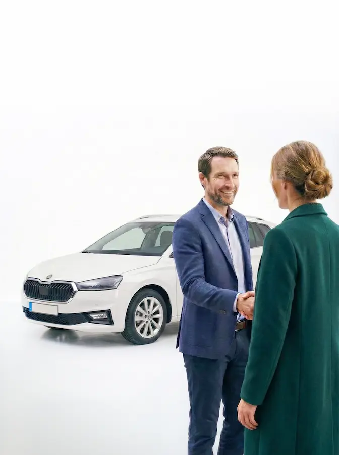 Un vendeur de La Fleur de l'Automobile qui serre la main à sa cliente devant le véhicule qu'elle vient d'acheter.