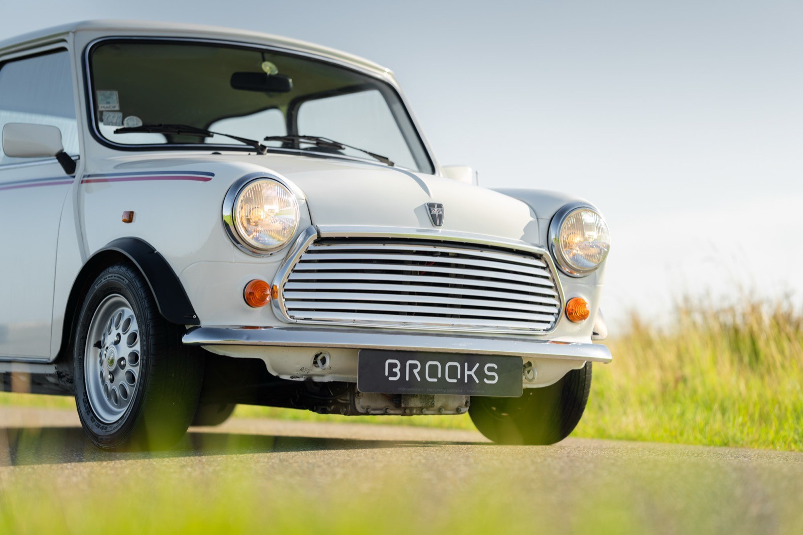 A classic white car parked in a grassy area with a clear sky in the background.
