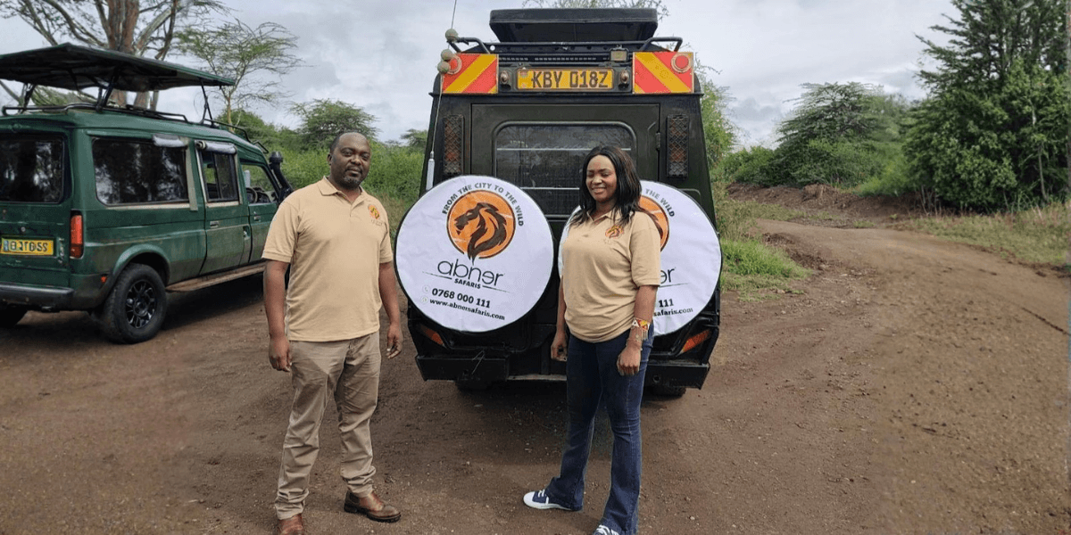 two safari guides, Robert Nyamwaya and a colleague, standing beside a safari vehicle with Abner Safaris branding.