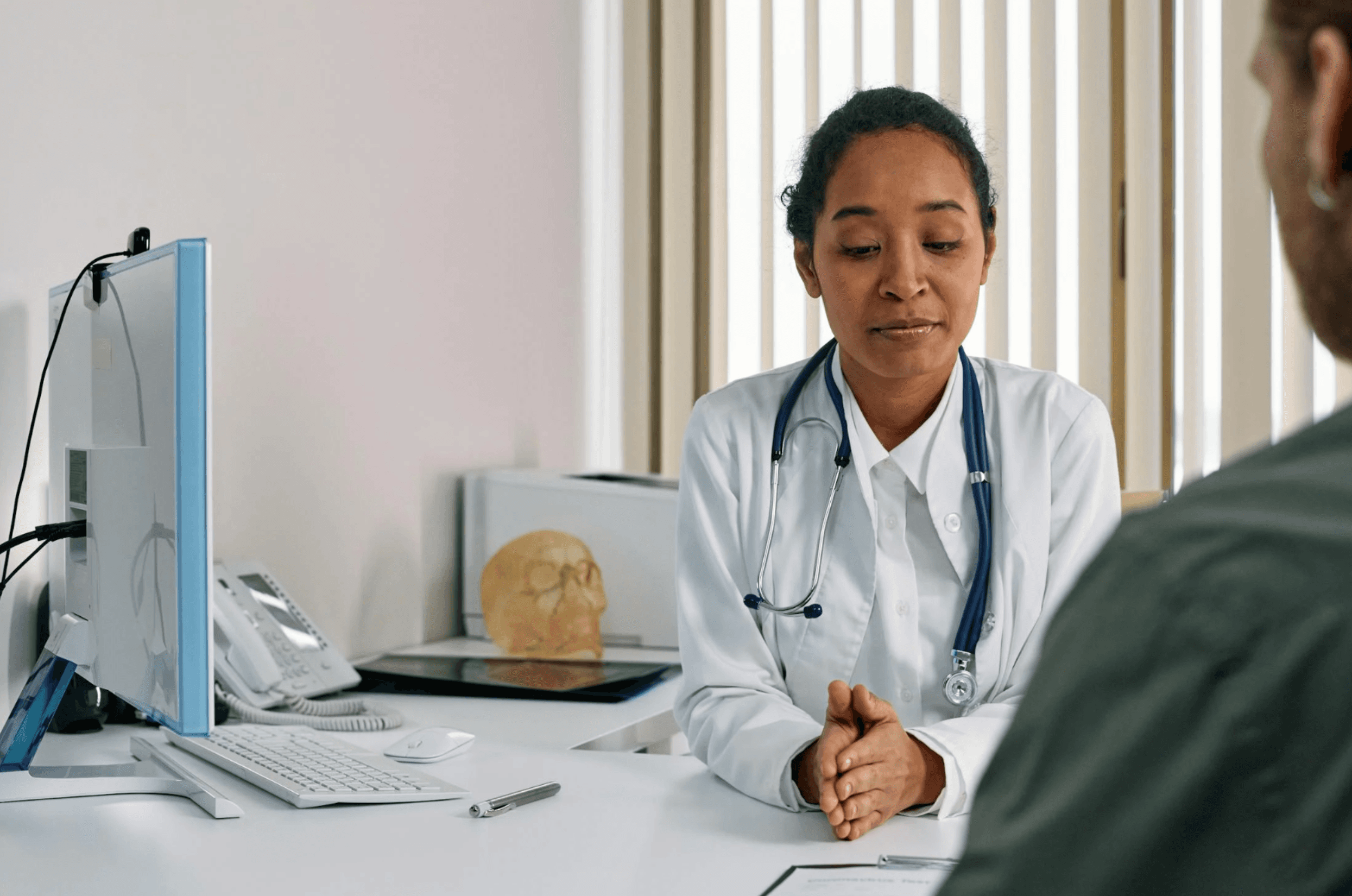 Woman in White Suit with Stethoscope Talking to a Person. Courtesy of Pexels