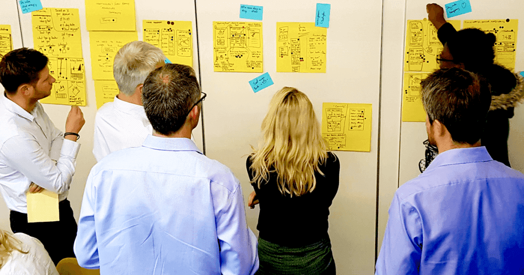 Group of professionals examining hand-drawn sketches and sticky notes on a wall during a corporate workshop