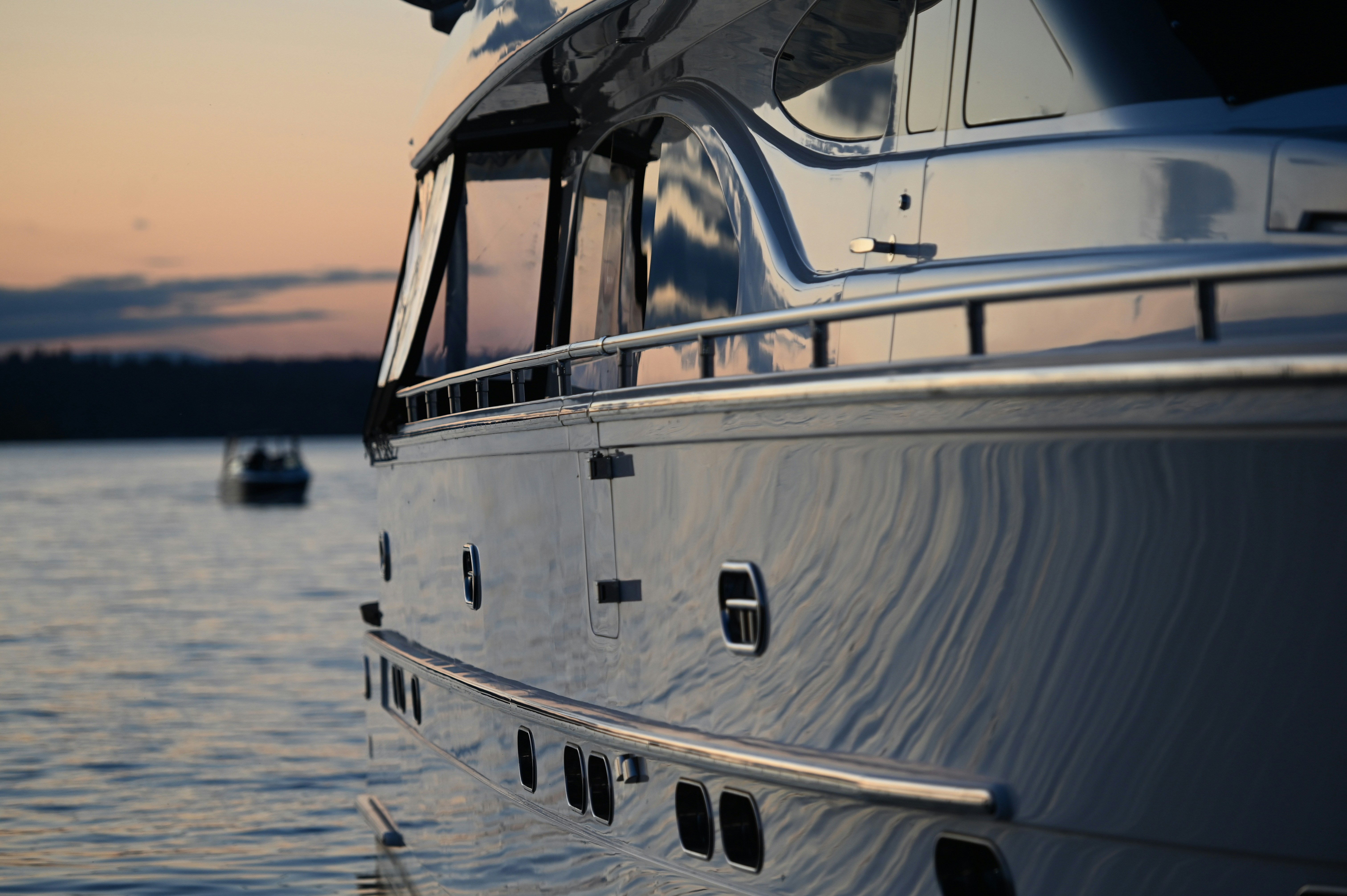 A sleek, modern yacht with reflective windows glides on a tranquil lake during a serene sunset, with another small boat visible in the background, showcasing luxurious nautical travel.