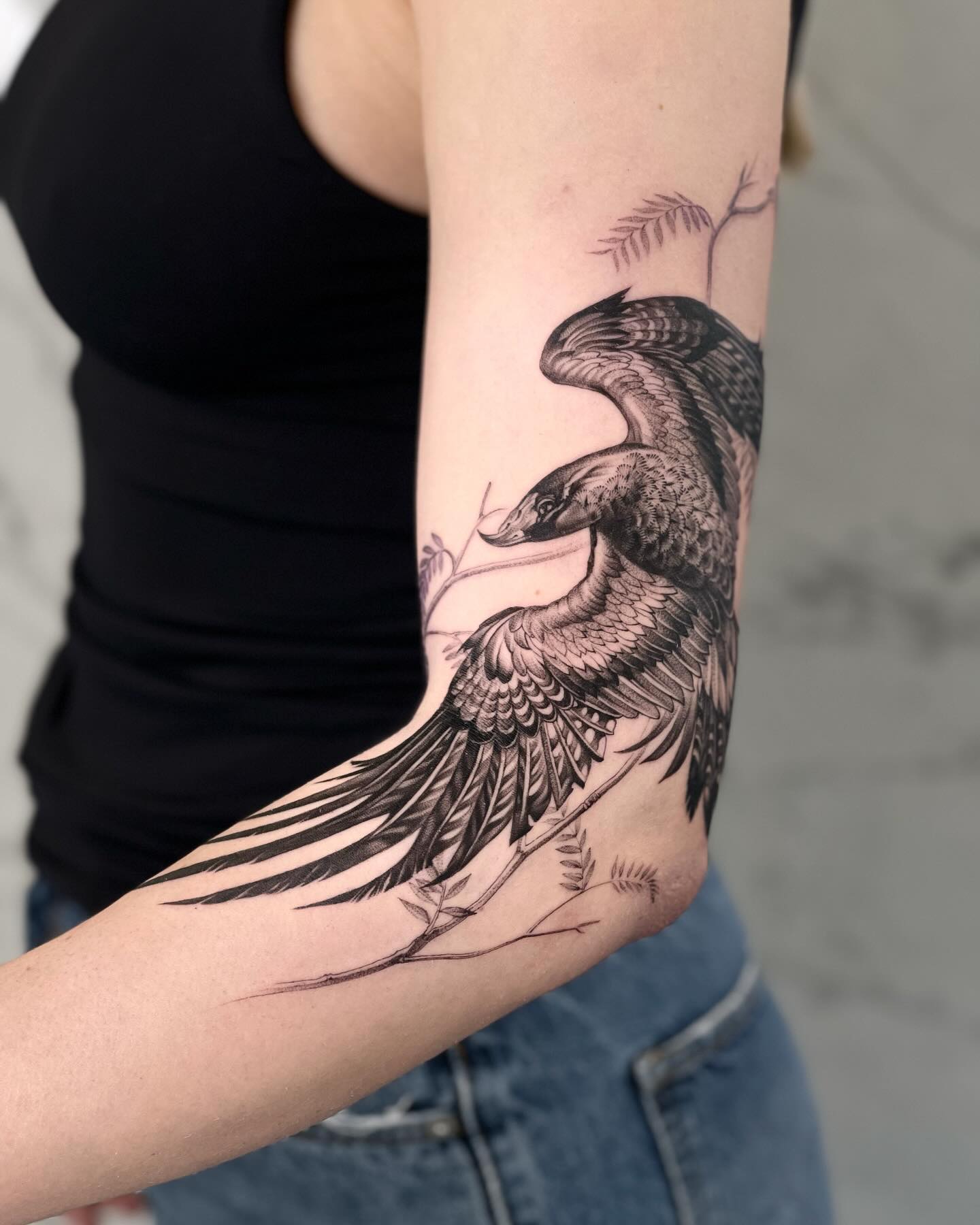 A woman's arm tattoo of a bird with outstretched wings, perched on a branch, covering her entire forearm.