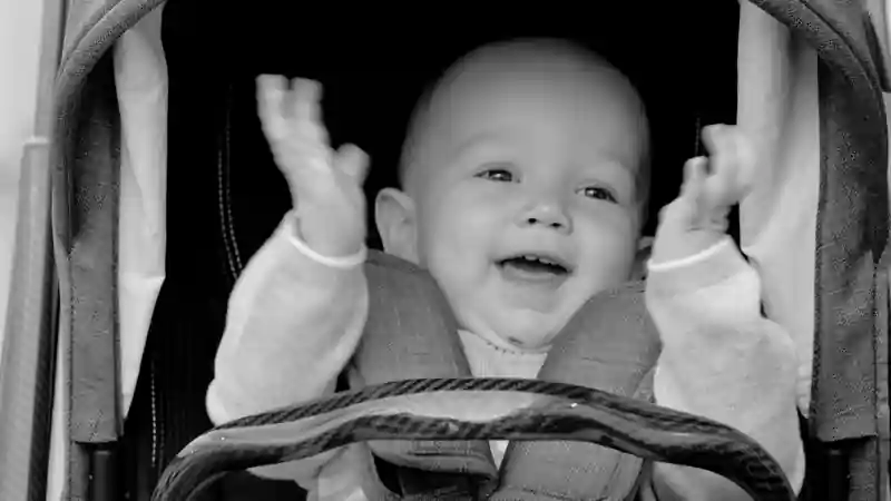 Black-and-white shot of a smiling baby sitting inside a JUNIORJONES stroller.