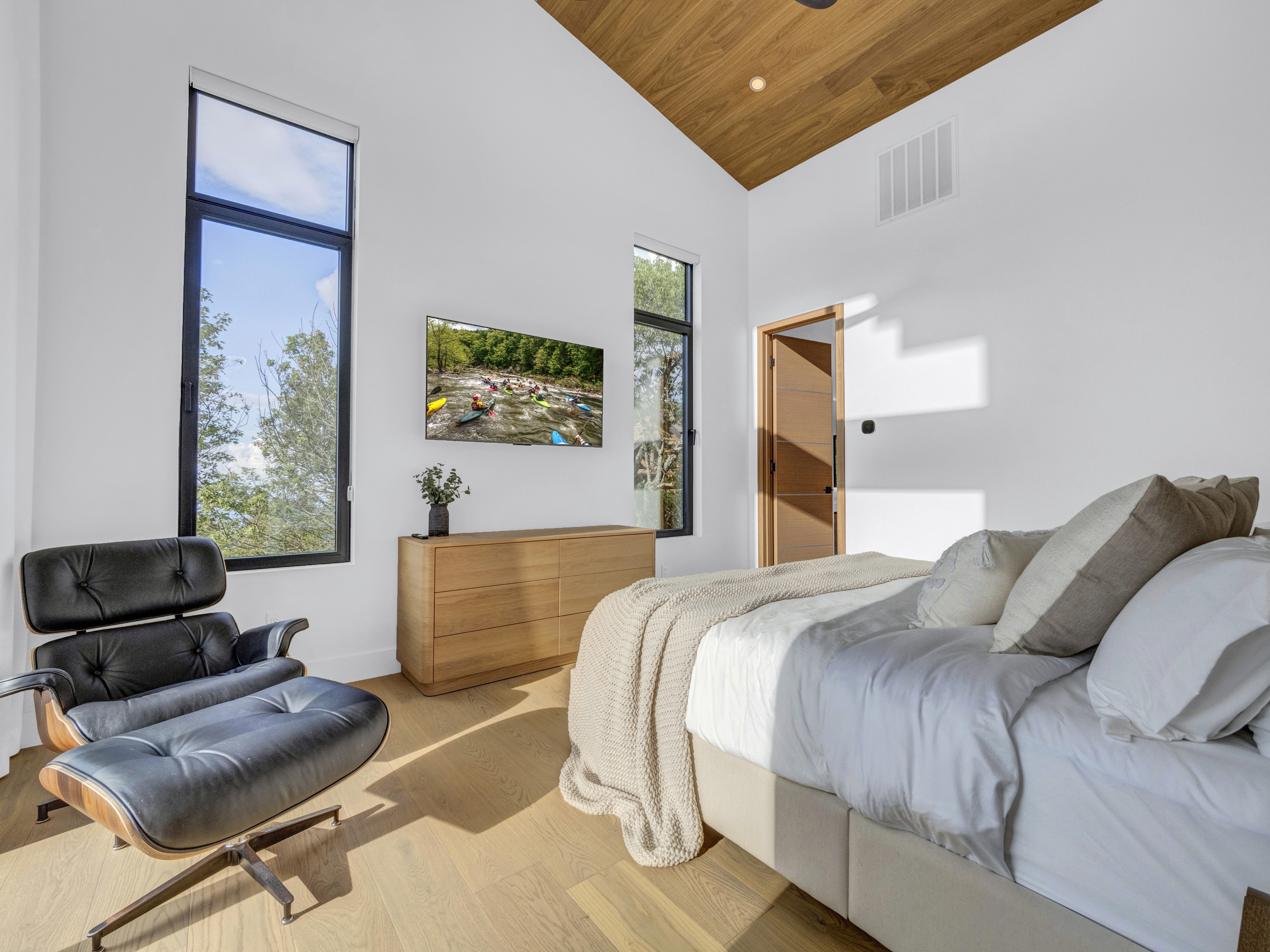 Upscale bedroom featuring an Eames-style lounge chair and ottoman next to tall windows with mountain views