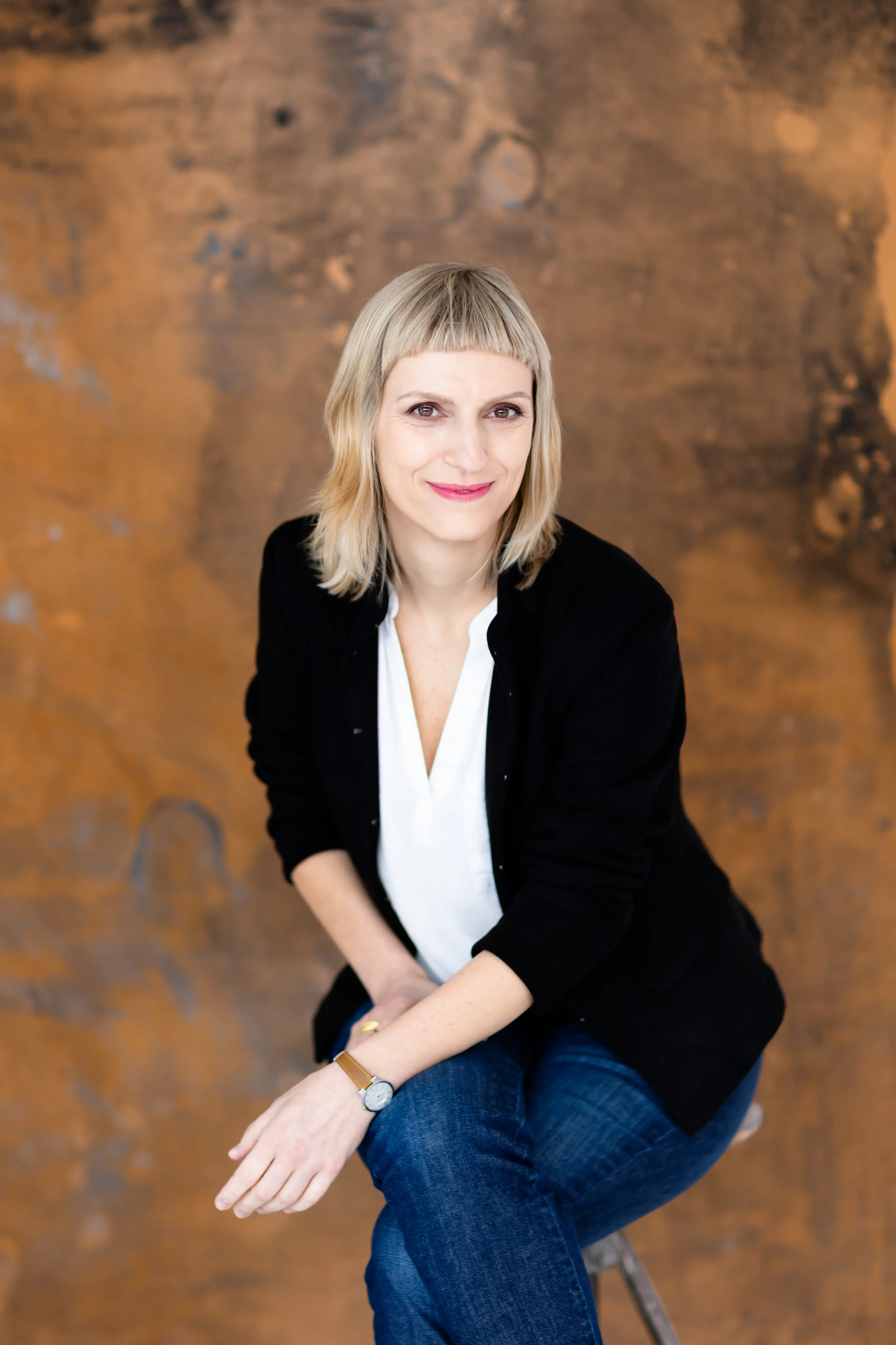 Siedząca na stołku kobieta z rękami na kolanach, wyrażająca spokój i kontemplację.