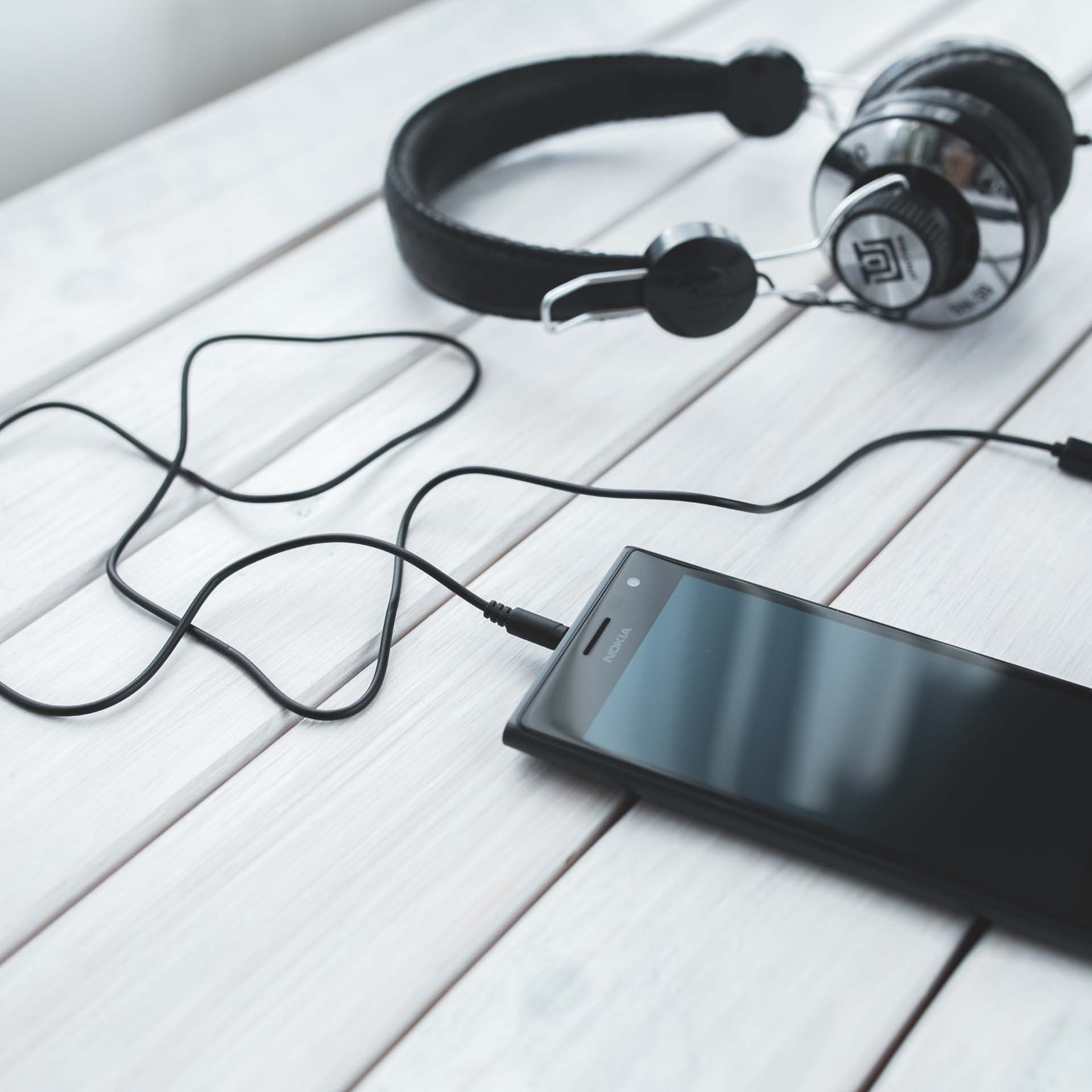 A Nokia smartphone connected via cable to black over-ear headphones resting on a white wooden surface.