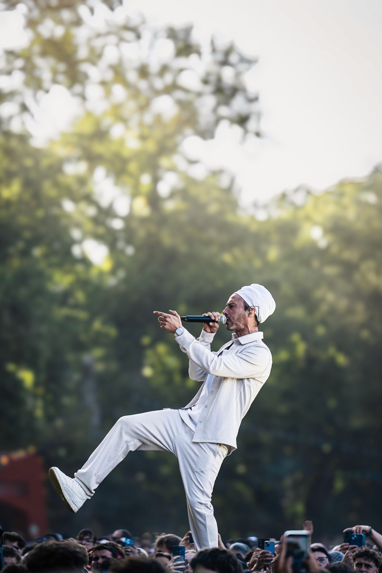 Chanteur en tenue blanche, jambe levée, en silhouette à contre-jour dans la lumière du soir.
