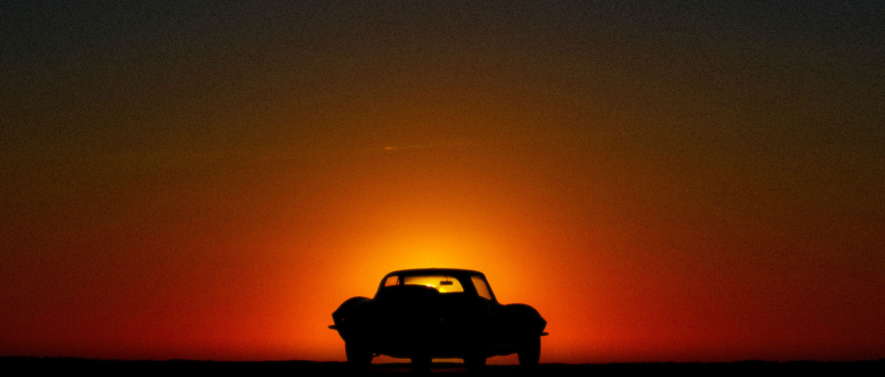 A red sports car parked in-front of a sunset.