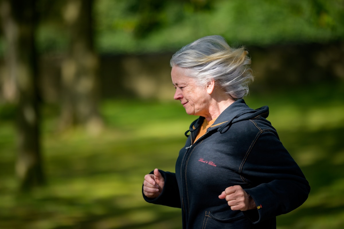 An older woman jogging outdoors in a green park, illustrating how staying active helps protect muscle and strength after 60.
