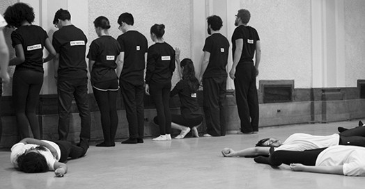 A black and white photo of a group of people, some facing a wall and some laying on the ground.