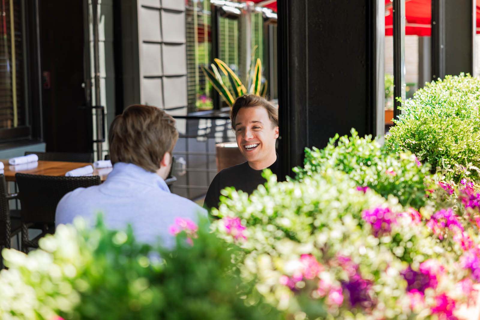 Two guests talking at a table behind flowering planters on the Patio at Hudson 29 Upper Arlington
