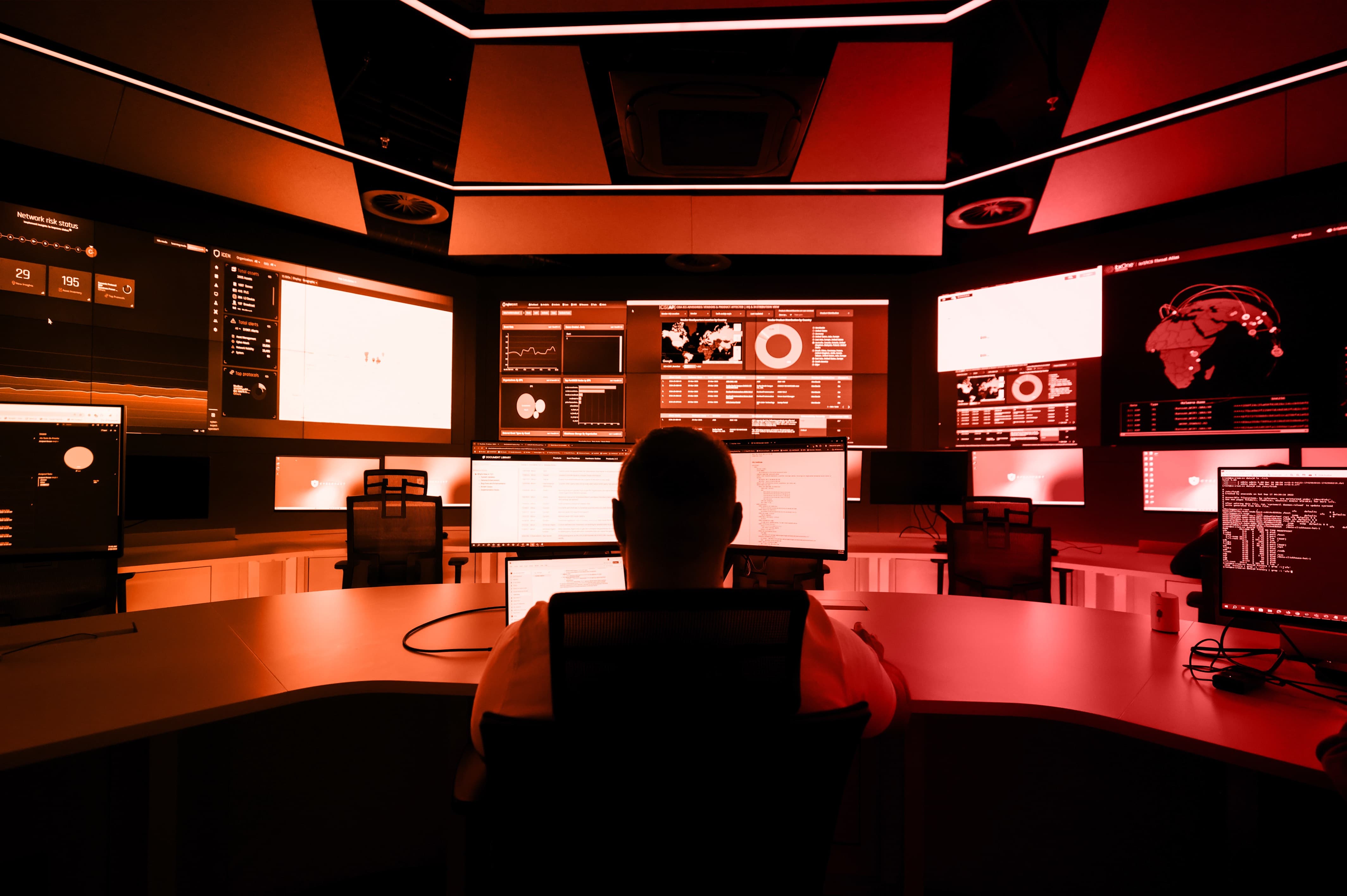 A person sits in front of multiple screens in a dimly lit control room, focused on the displays.