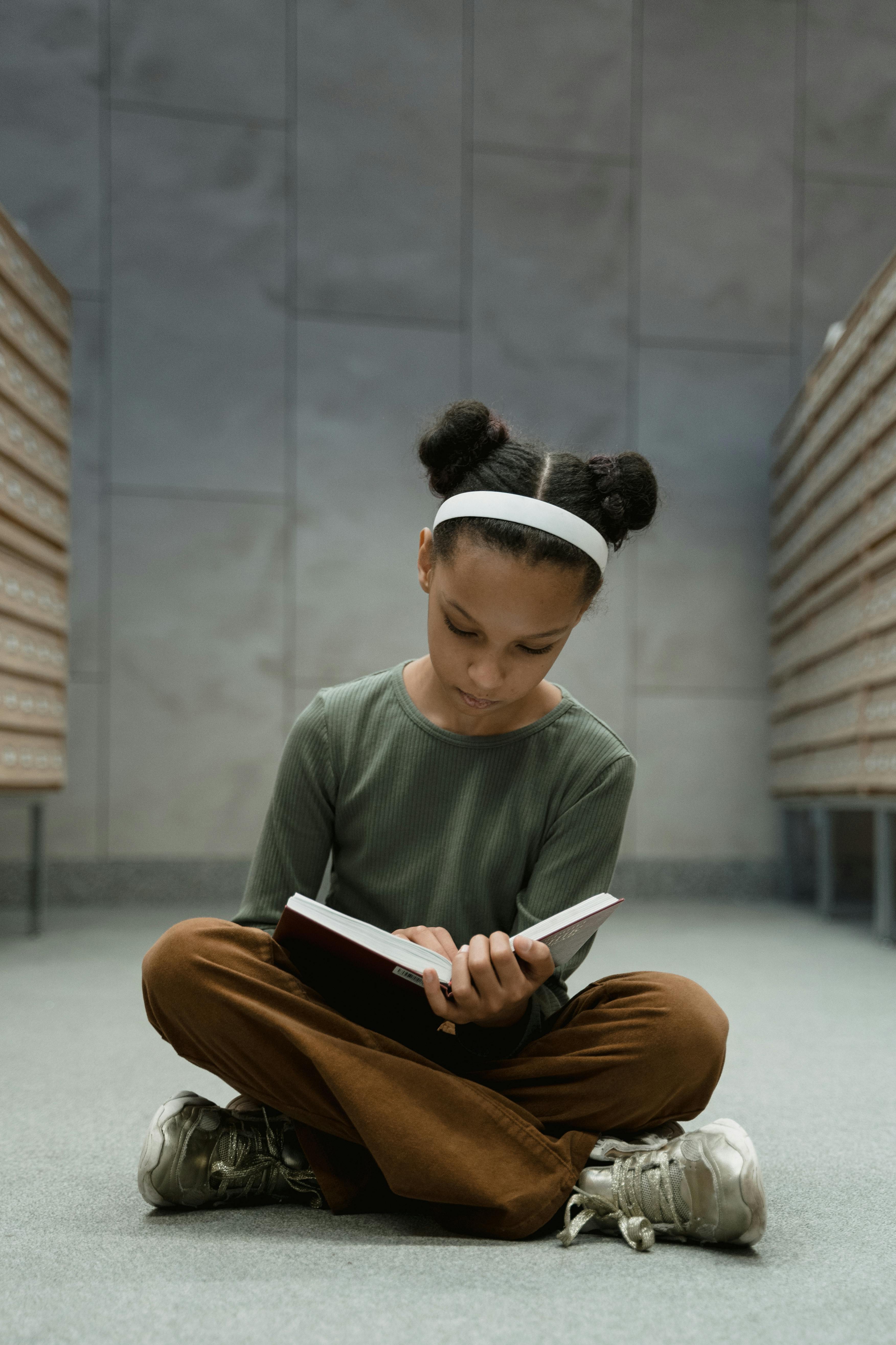 A student wearing a red uniform sits while holding a book in his hands