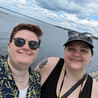 My wife and I smiling, with sunglasses overlooking a beautiful Maine waterfront. It's picturesque!