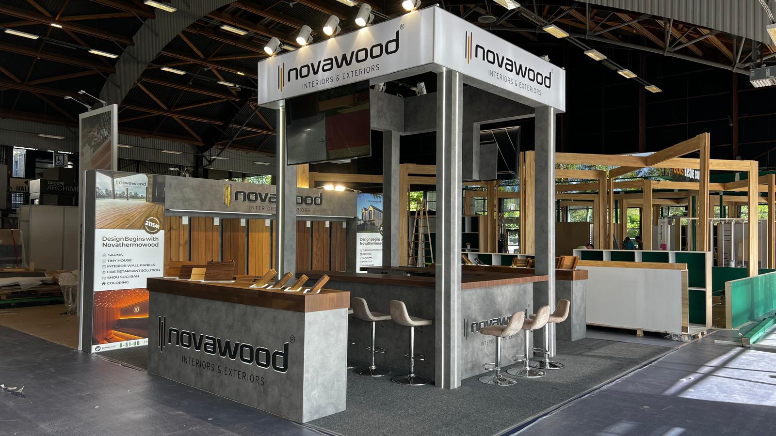 Novawood exhibition stand at Timber Show 2026 Nantes, featuring an elevated branded header, illuminated columns, and grey concrete-effect surfaces with warm wood finishes.