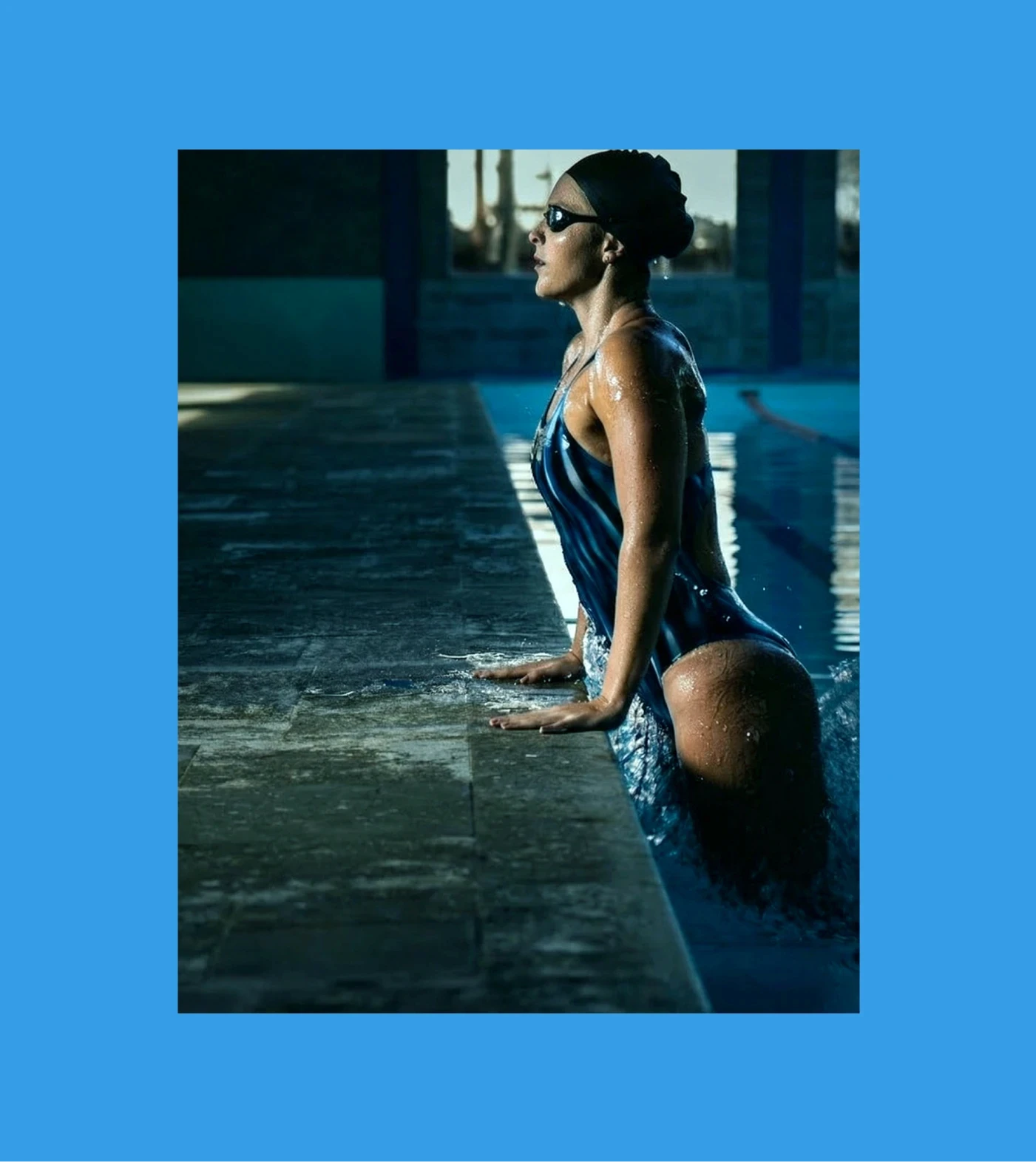 Nadadora saindo da água na borda da piscina, usando traje azul marinho, fundo azul vivo — campanha Fabiola Molina