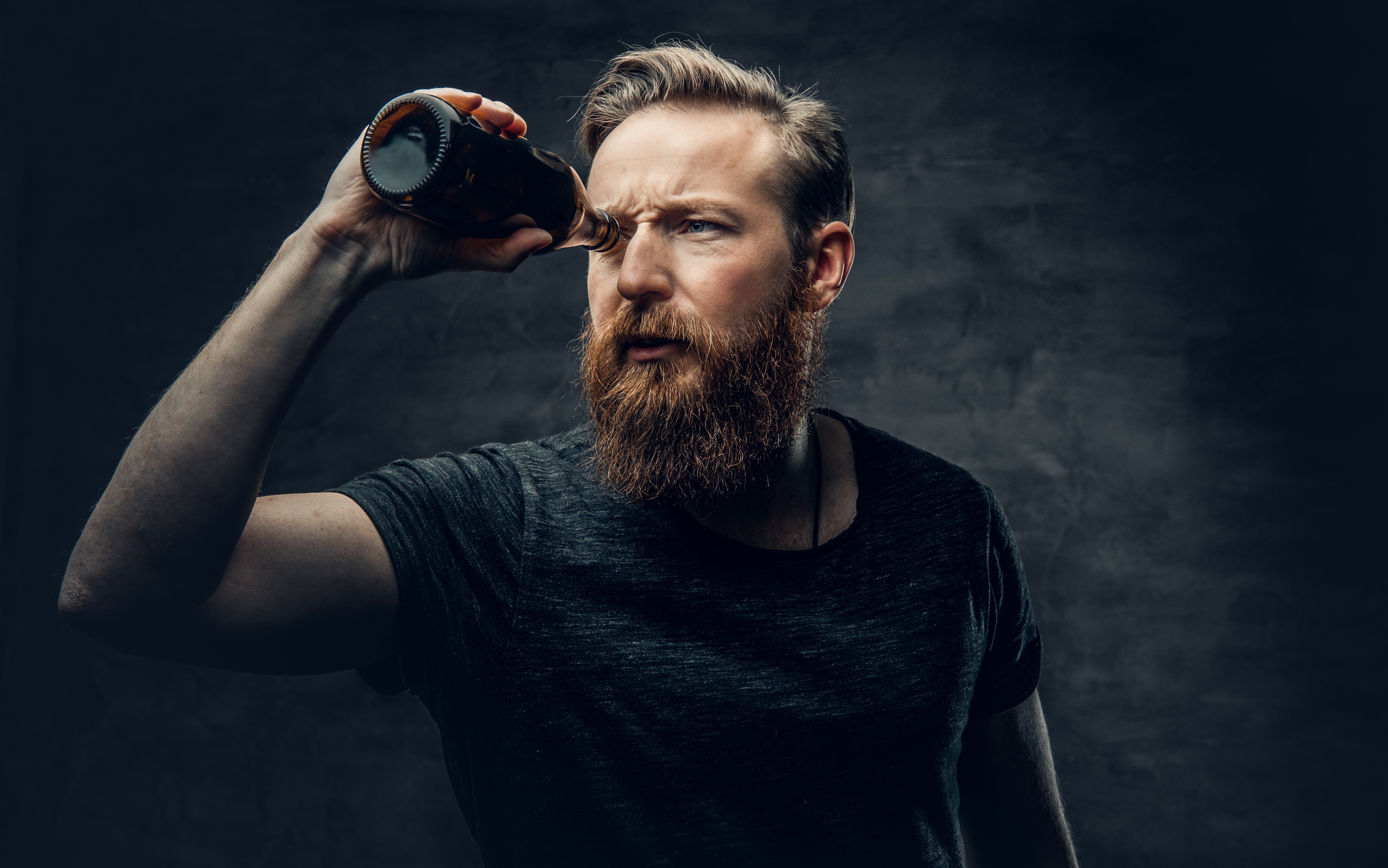 man holding beer bottle over eye like a spyglass
