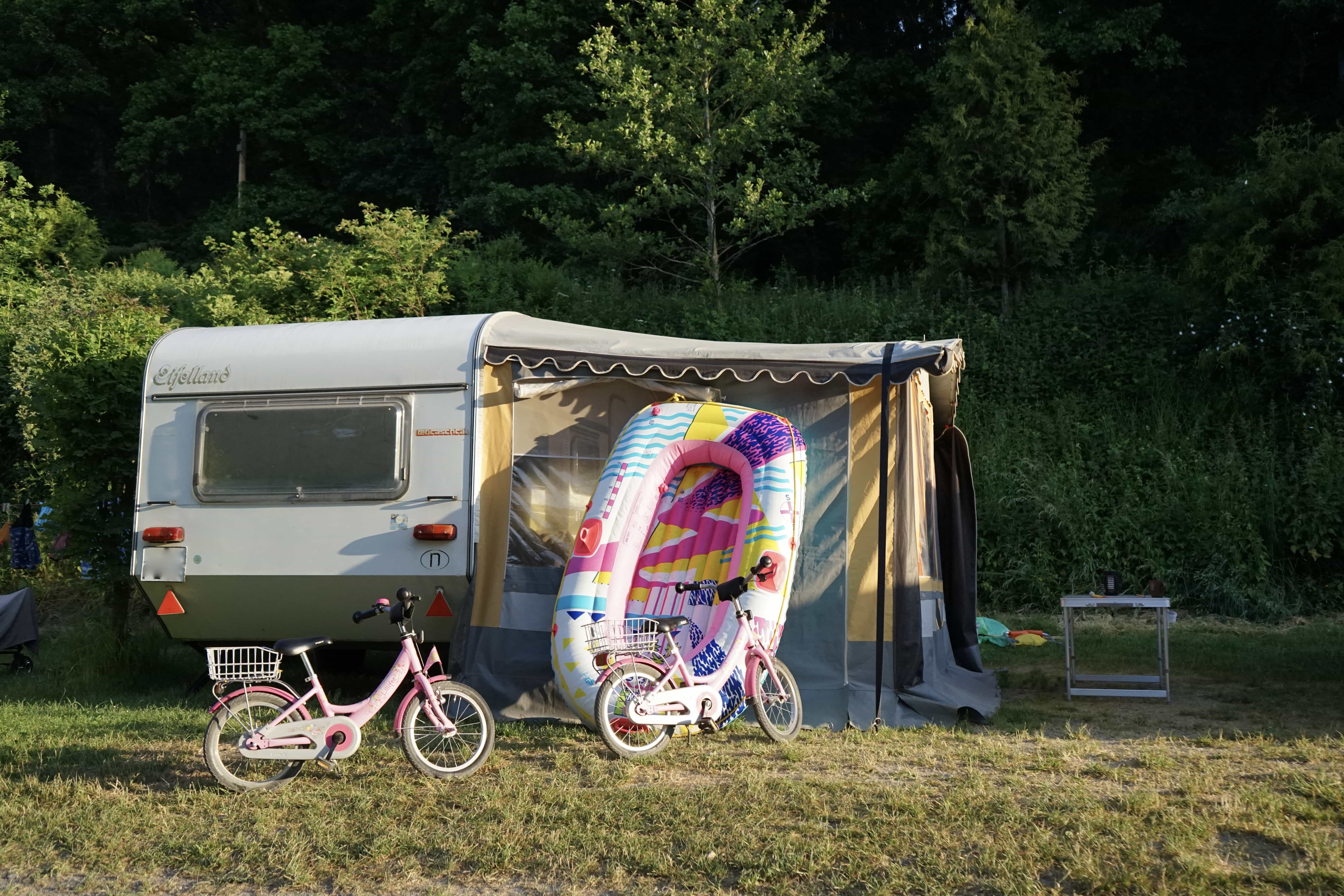Wohnwagen mit Schlauchboot und zwei rosa Kinderräder
