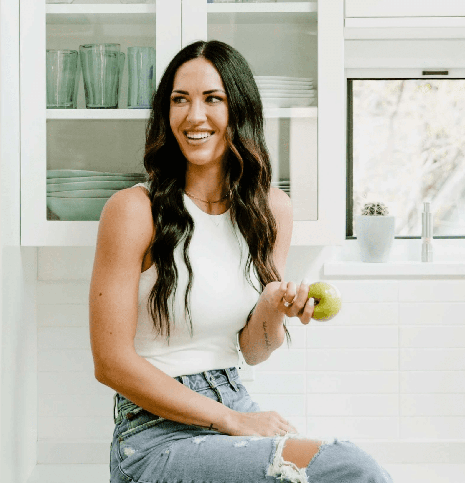 Shae Davis sitting in a bright kitchen holding a green apple,