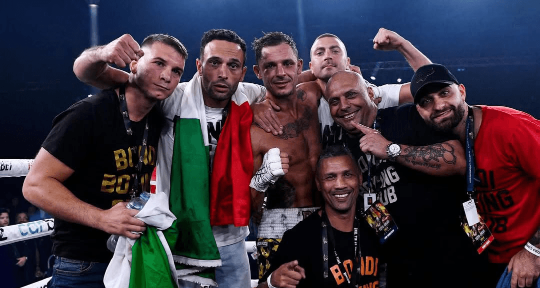 Danilo Dash Creati surrounded by his team holding flags and celebrating after a fight.