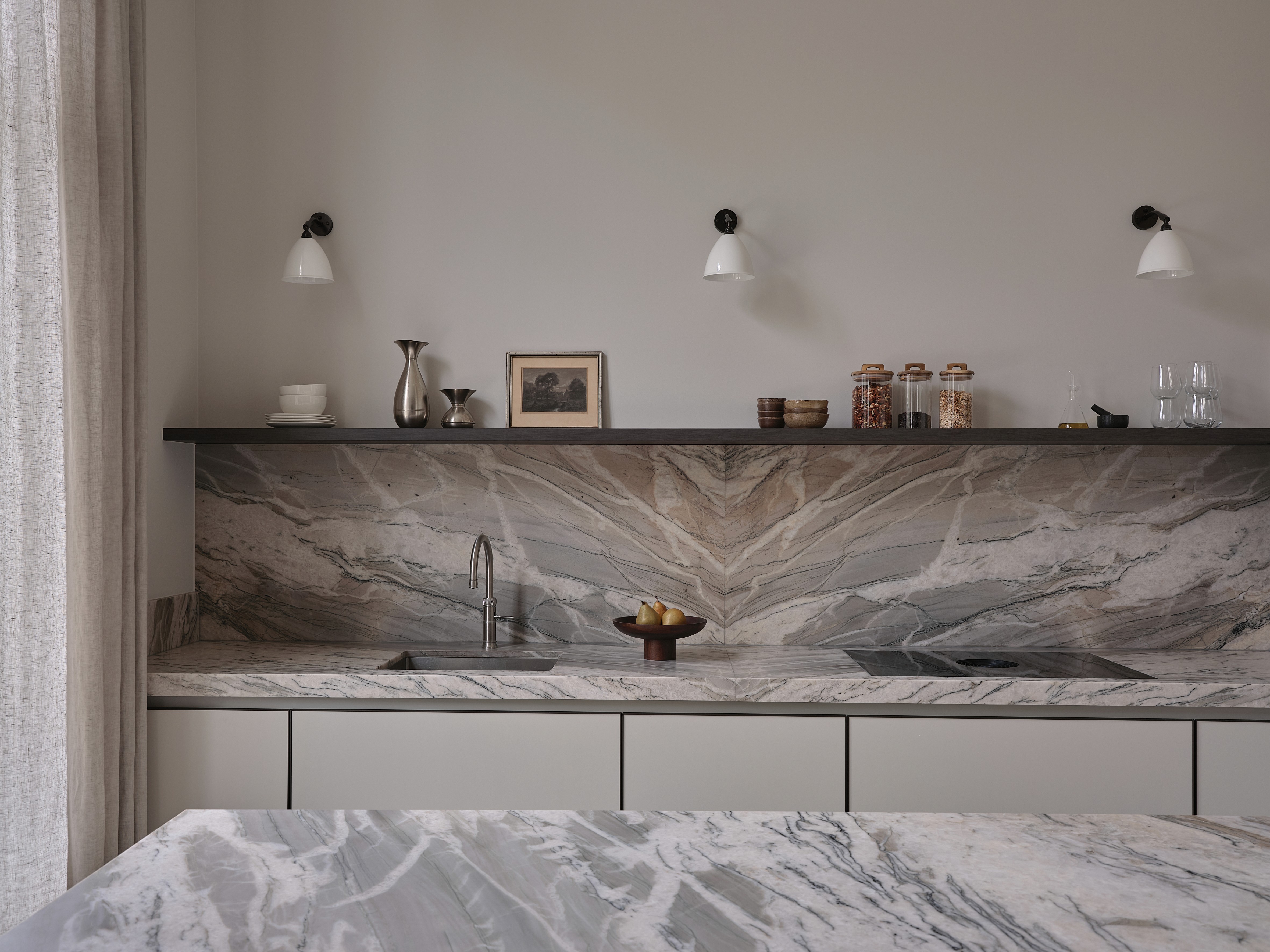 Kitchen detail showing dramatic veined quartzite backsplash with integrated sink and white wall sconces