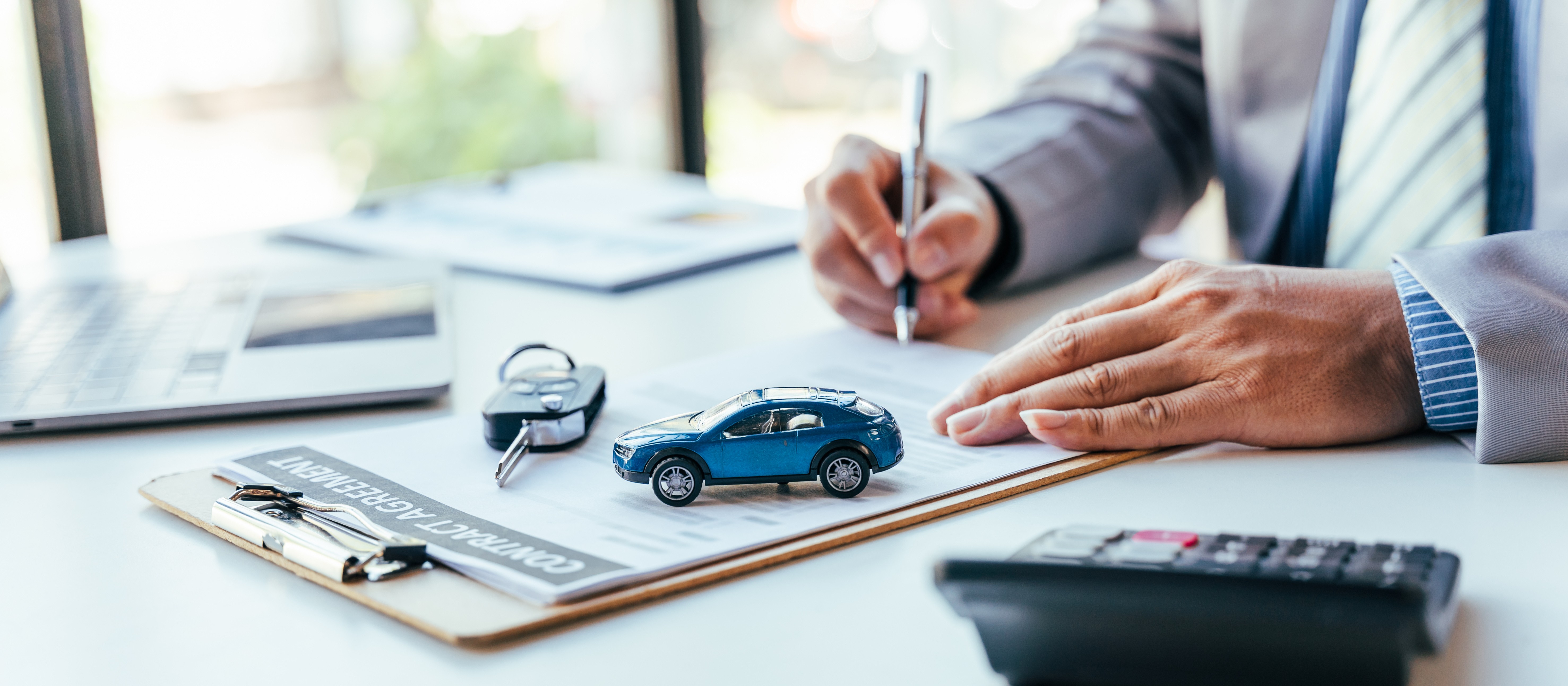 Person signing car contract with toy car, keys and calculator on table. Car insurance or purchase.